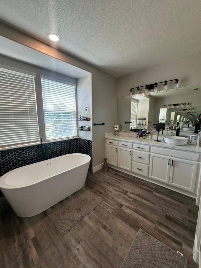 Modern bathroom with a freestanding bathtub, stylish bathroom cabinet design in the double-sink vanity with mirrors, wooden flooring, and large windows letting in natural light.